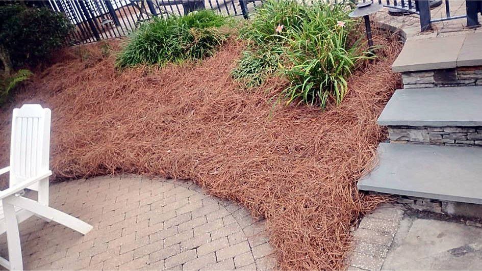 Pine straw bed beside a paver patio, white chair and stone steps