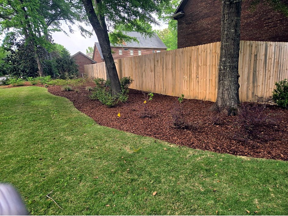 Edged lawn with a mulched bed along a wooden privacy fence
