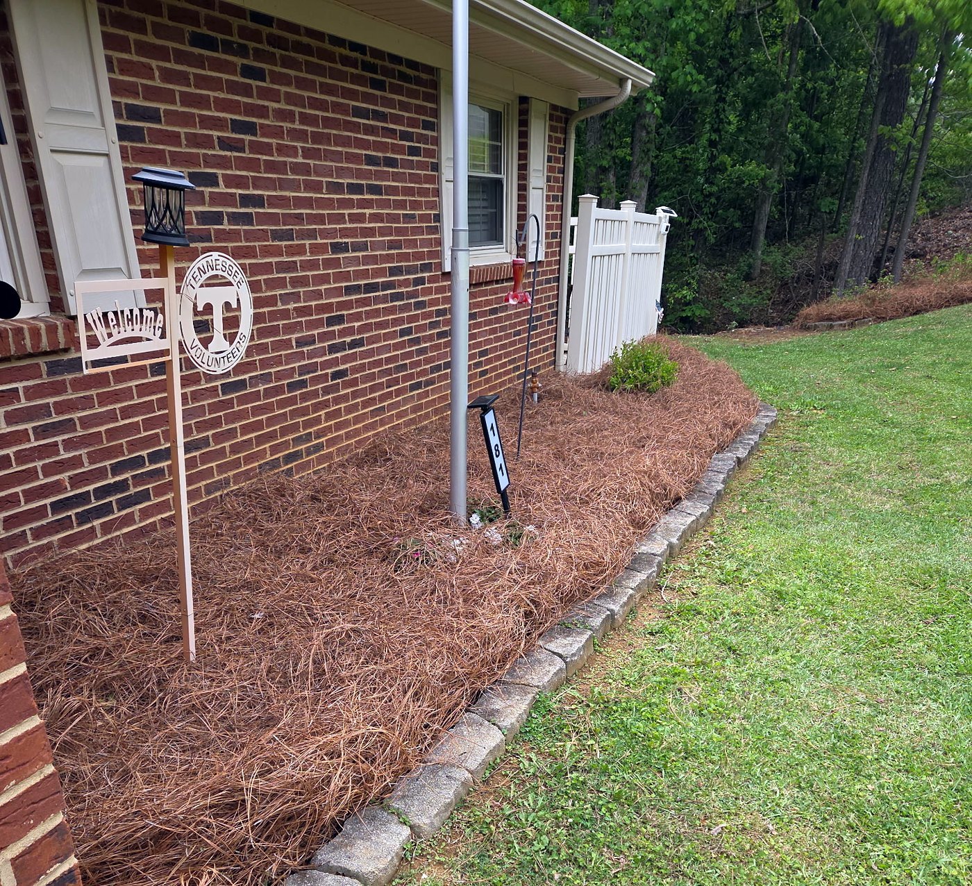 Fresh pine straw bed with stone edging along a brick house beside the lawn