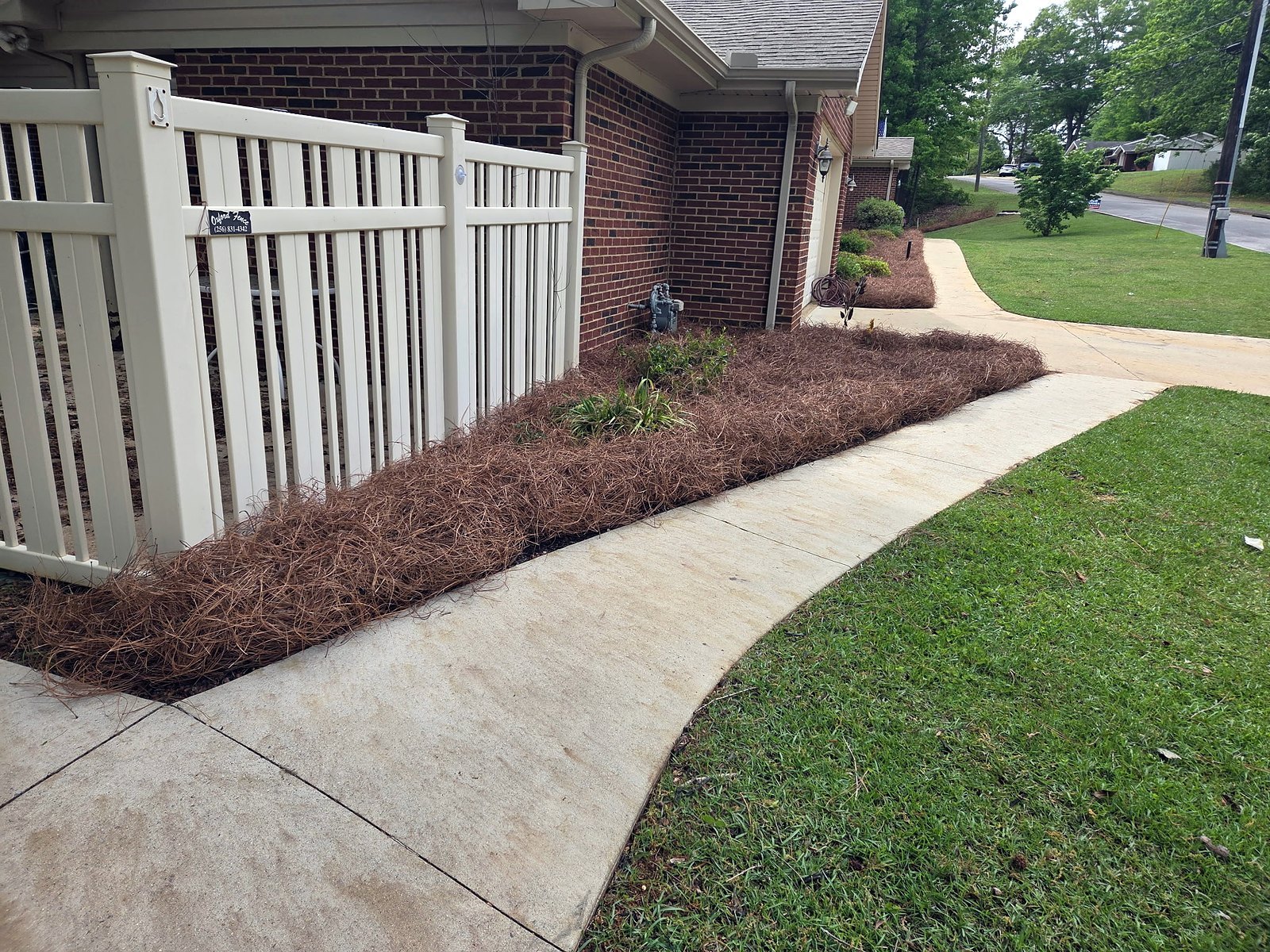 Edged lawn and sidewalk with a pine straw bed running to a white fence