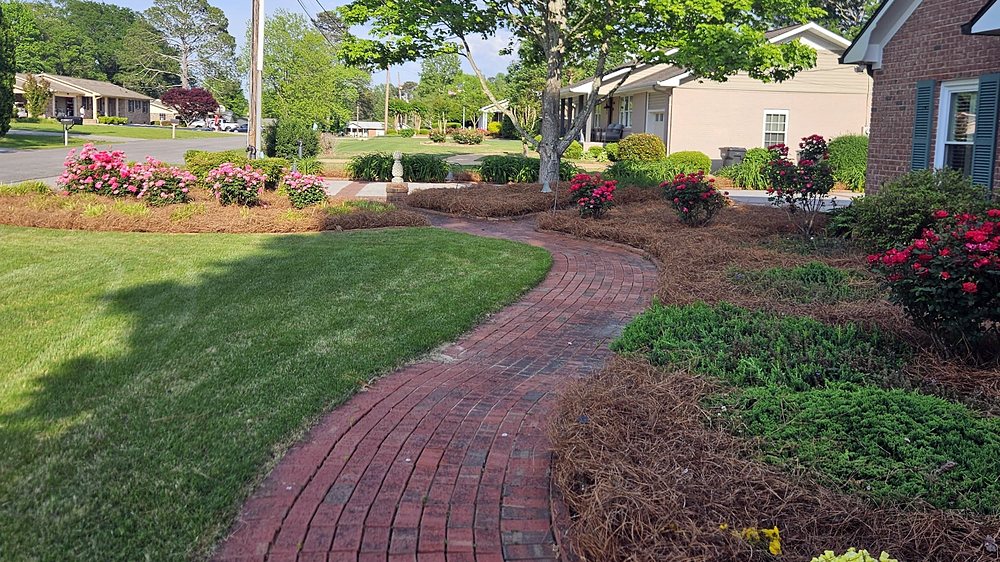 Curved brick walkway between a mowed lawn and pine straw beds with roses in bloom — a Garcia job